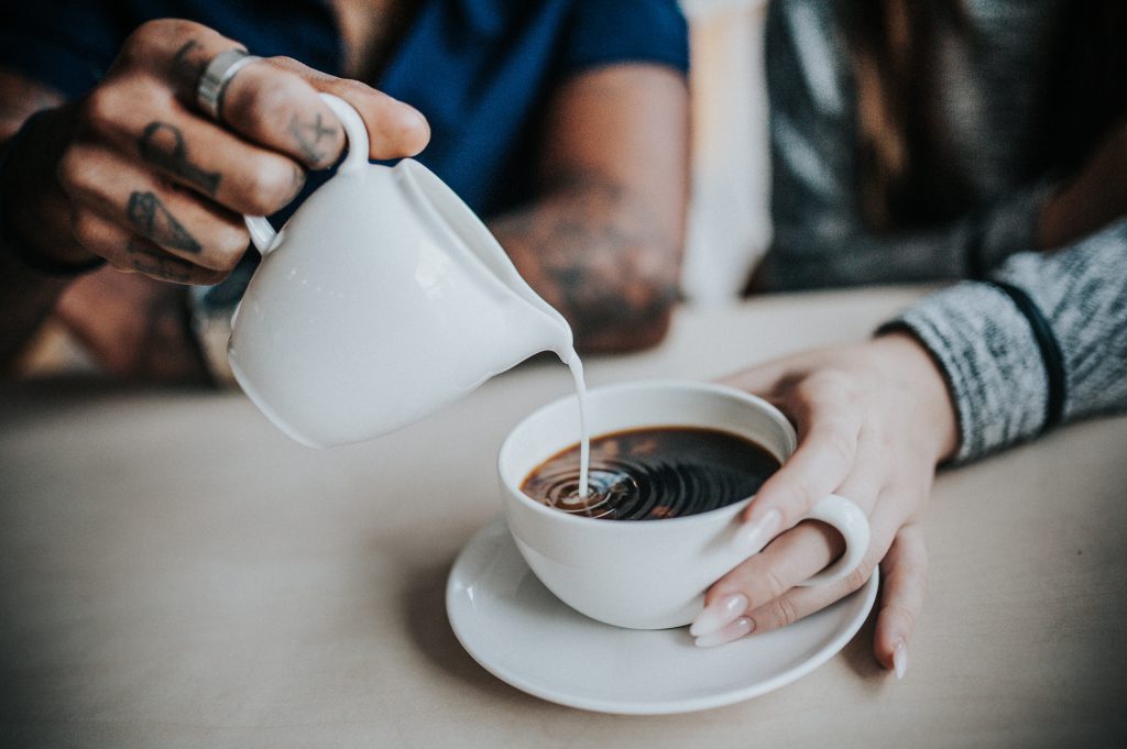 How do we begin building a friendship across a boundary of division? We first must establish a rapport with that person who sees the world differently to you. In this photo, a man's tattooed right hand pours milk into a coffee cup being held by a woman of a different race. She has long fingernails and no tattoos, the difference between the two is very obvious.