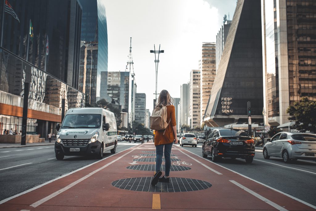 A young woman with a backpack walks gingerly in the middle of a bike lane set inside the main road of a busy city street. When pain comes, we can chose to look toward the pain, or to look toward the hope and stay focused on that.