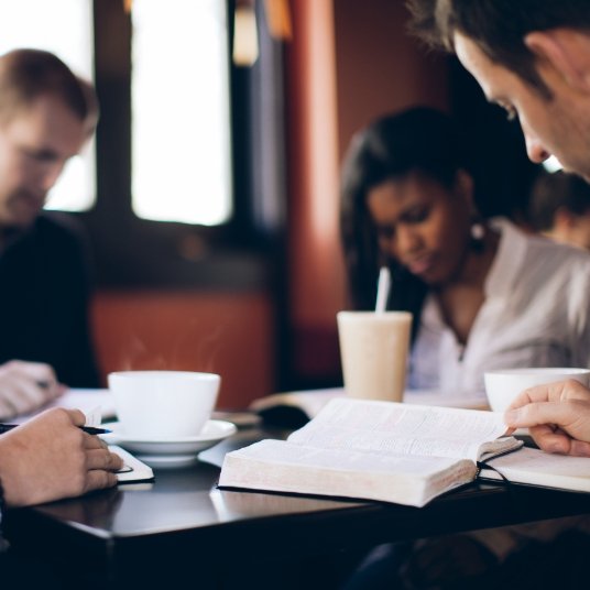 Two men and a woman sitting at a table reading the Immerse Bible