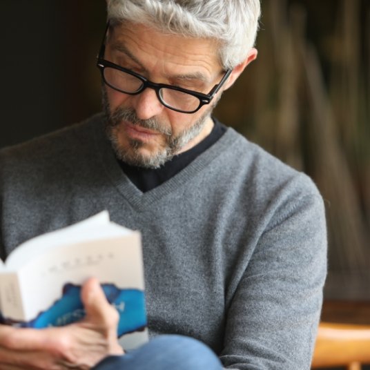 A middle aged man with glasses sitting cross-legged and reading Immerse: Messiah