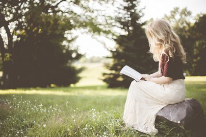 Pretty young blonde woman in profile sitting down and reading a book outside