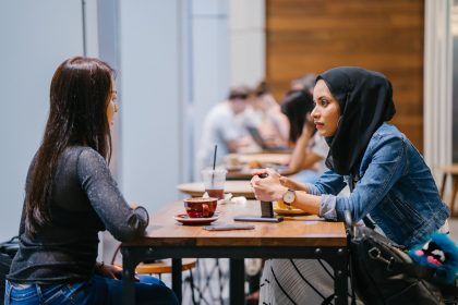 Young woman wearing burka sitting at table talking to another young woman with tea