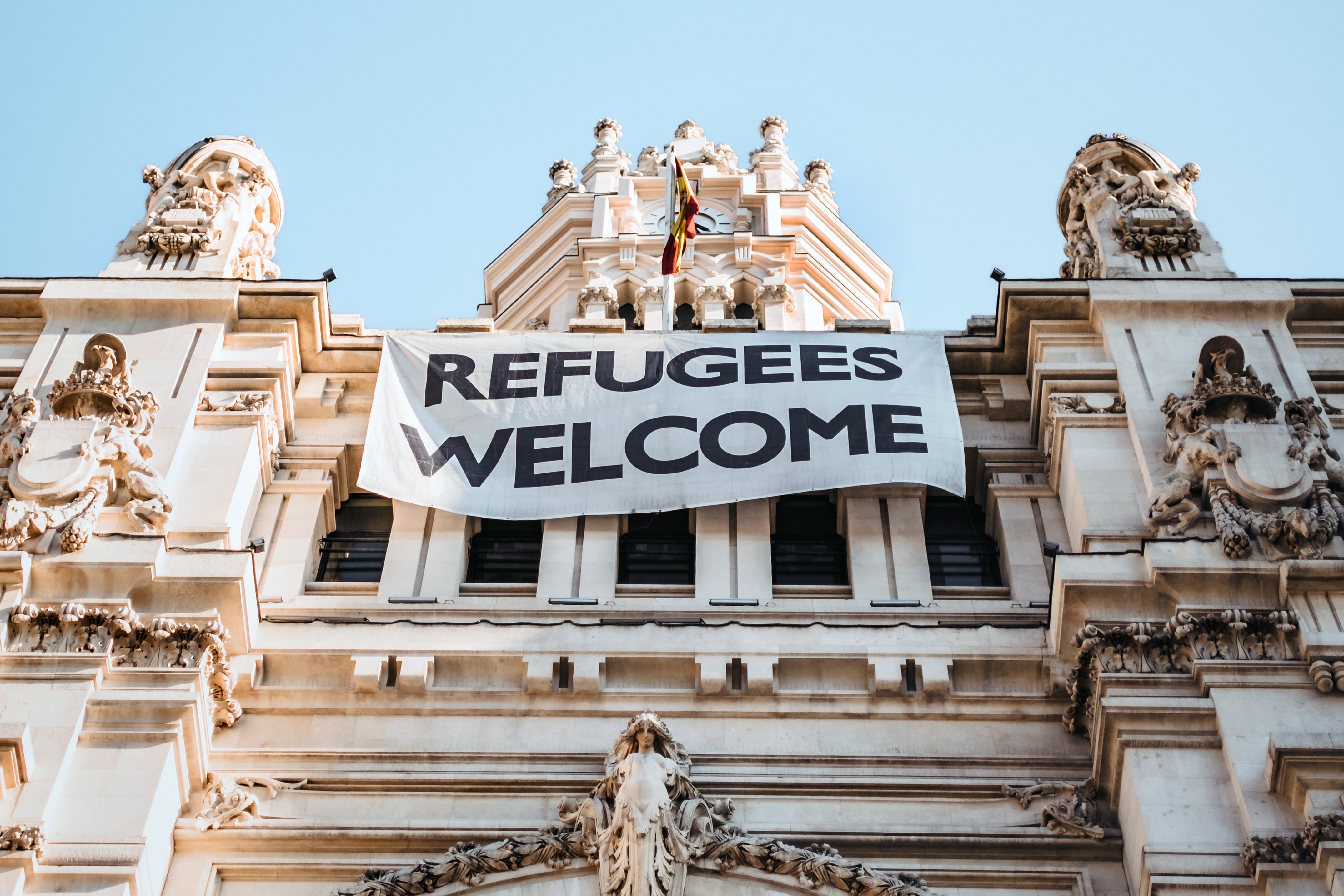 White building exterior architecture with sign that says "Refugees Welcome"