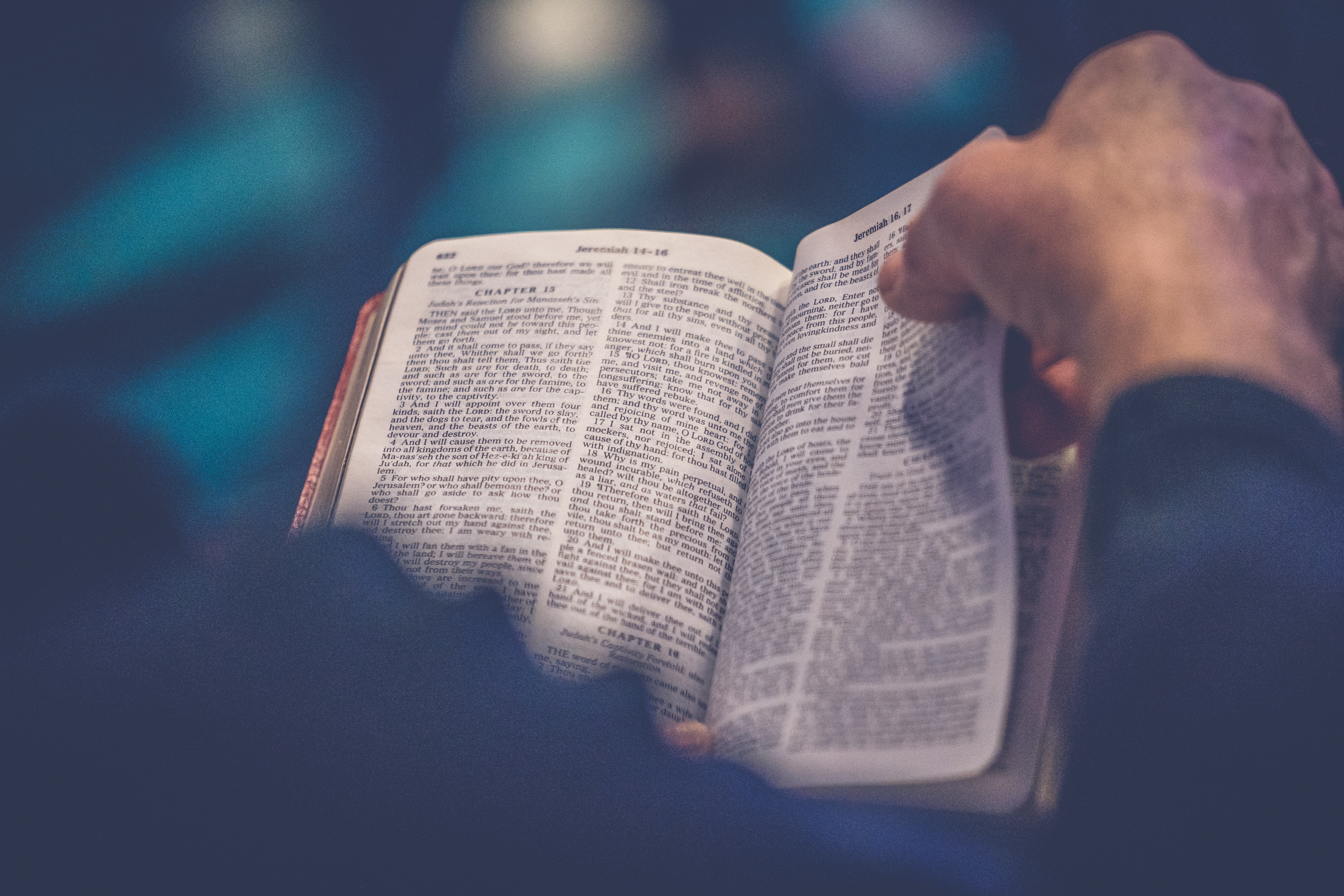 Close-up from behind of man's hand turning pages of Bible