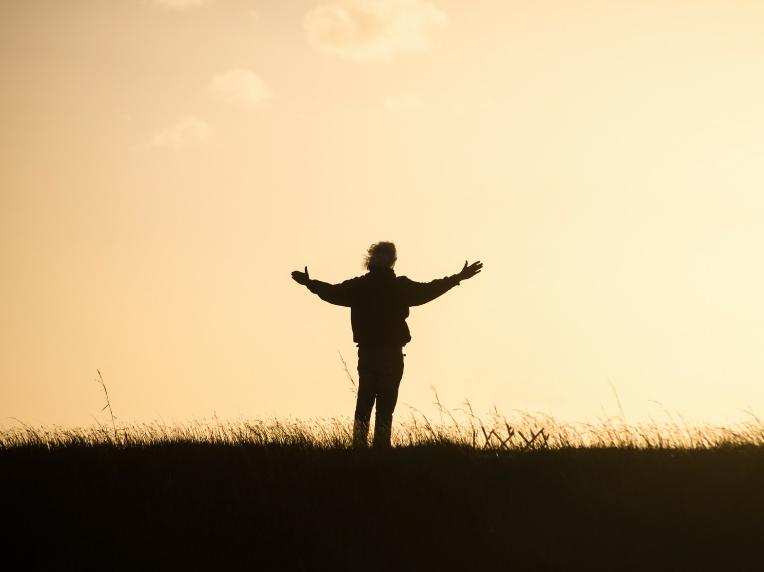 person standing outside at sunset while holding hands out