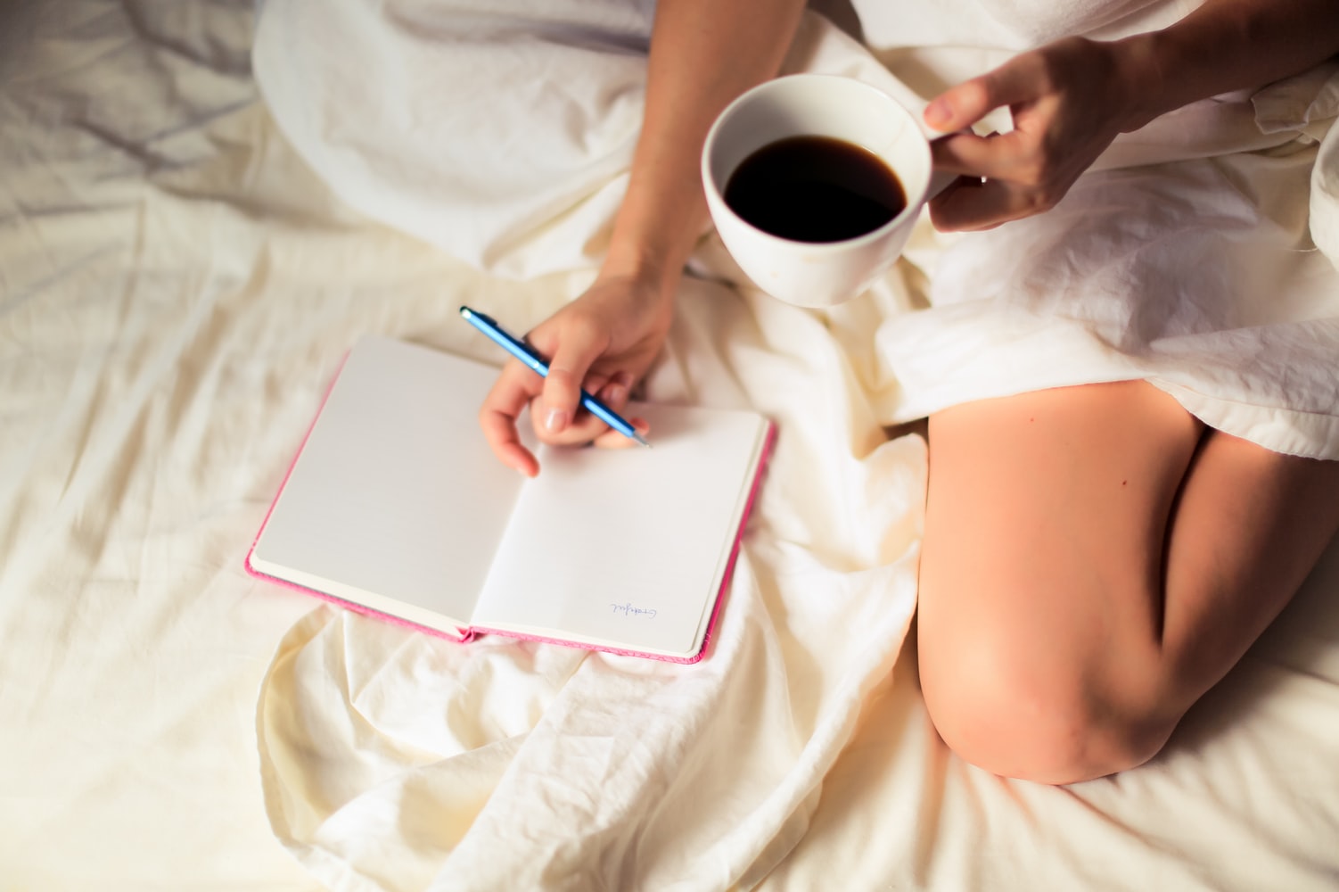 woman journaling with coffee cup on bed
