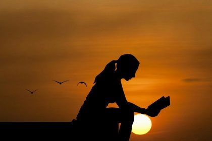 silhouette of young woman sitting and reading with setting sun in background