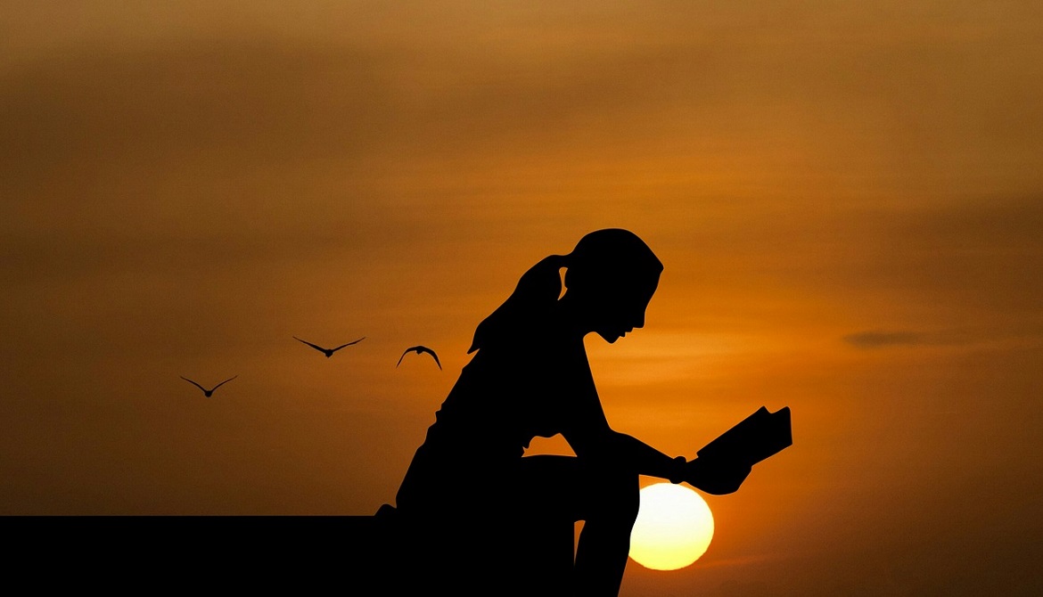 silhouette of young woman sitting and reading with setting sun in background