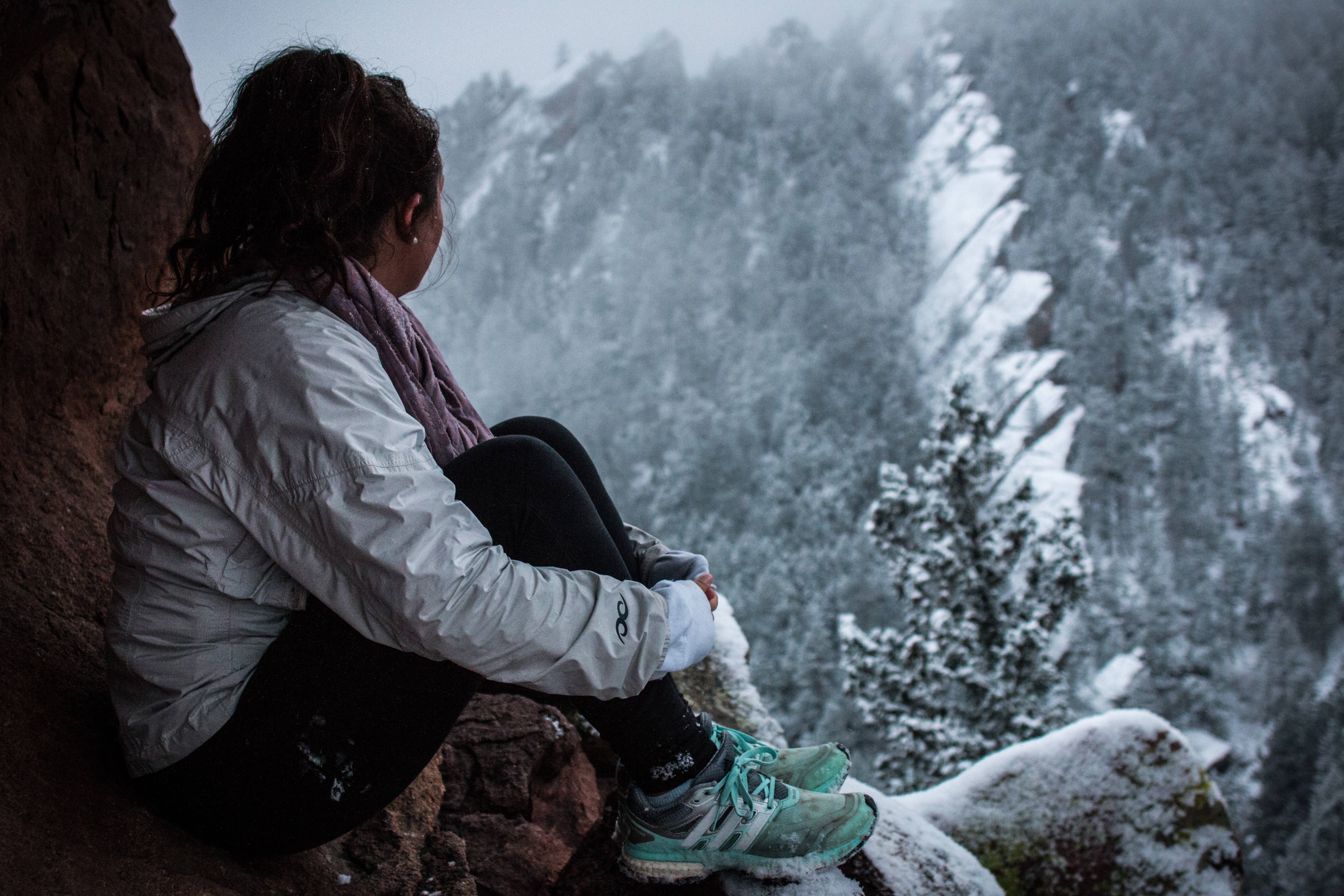 Young woman with dark hair wearing a winter coat and sneakers, looking out over a winter landscape