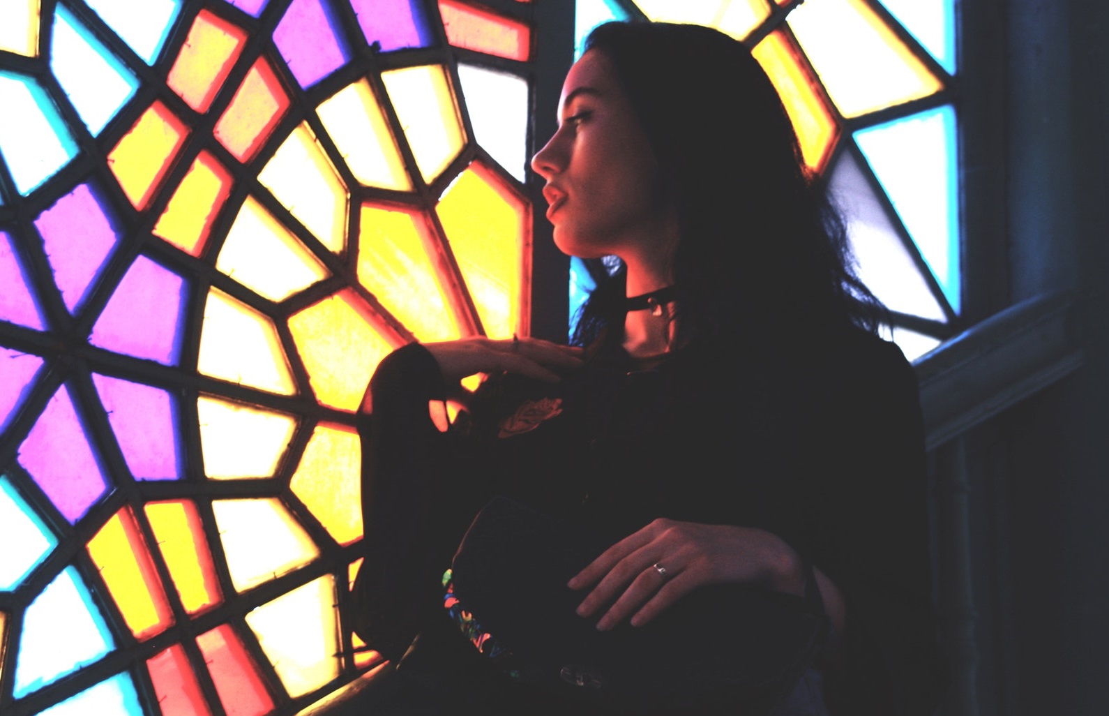 Beautiful young woman with dark hair looking at a backlit stained glass window
