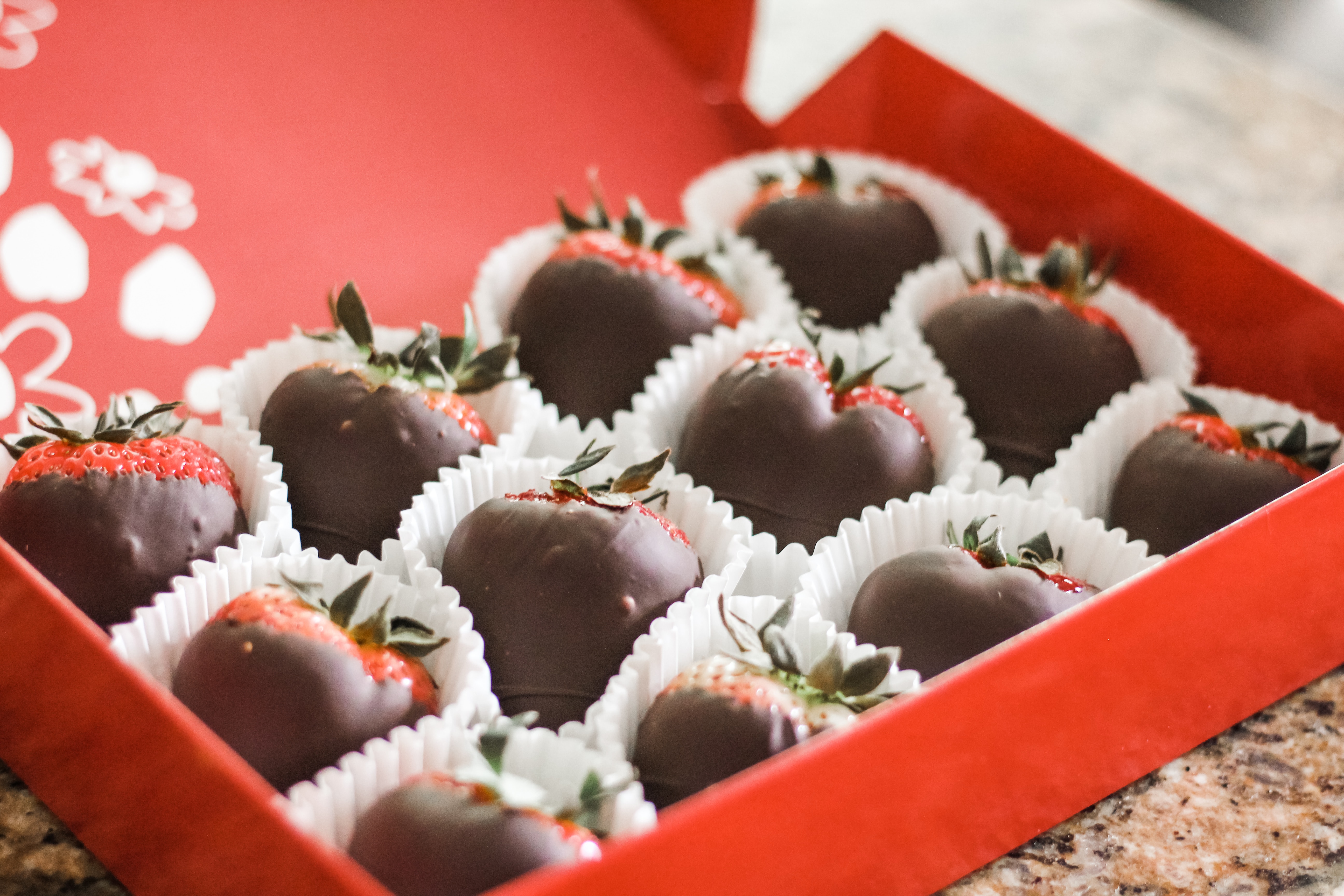 Red Valentine's box full of chocolate dipped strawberries in white wrappers
