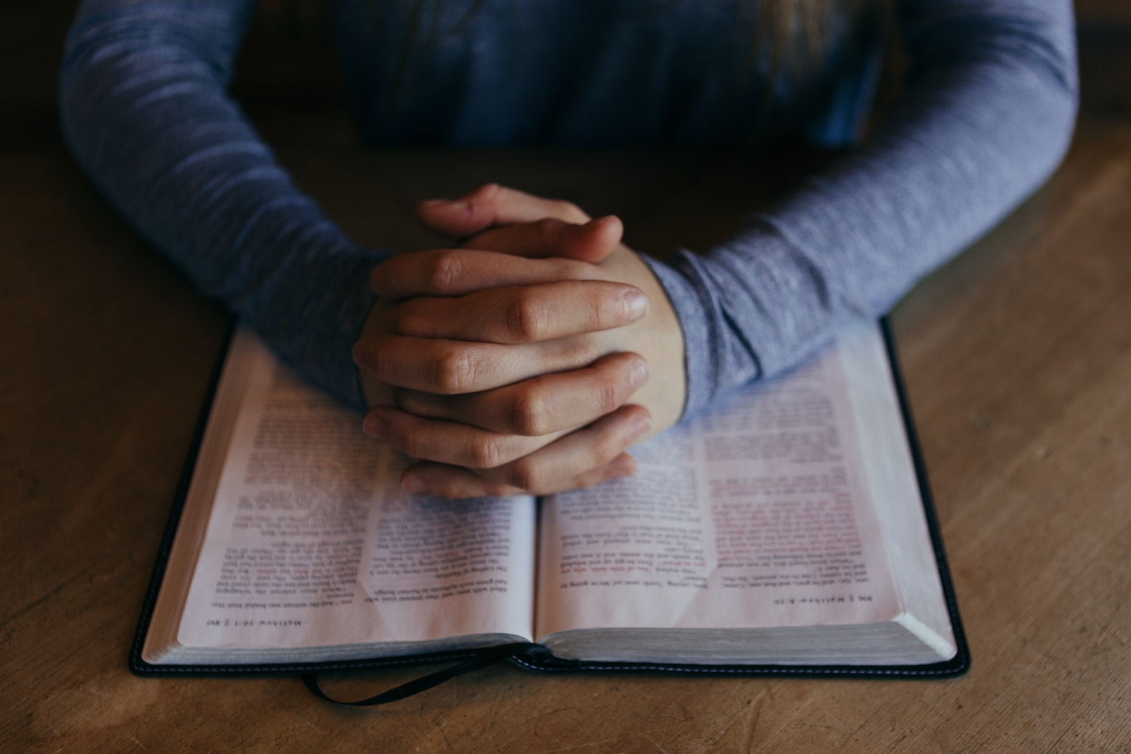 person praying with hands folded across bible