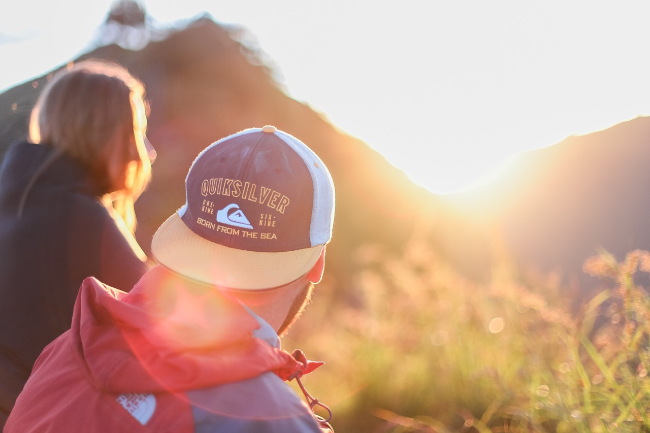 A young man and woman outside looking at the sun rising over the hills