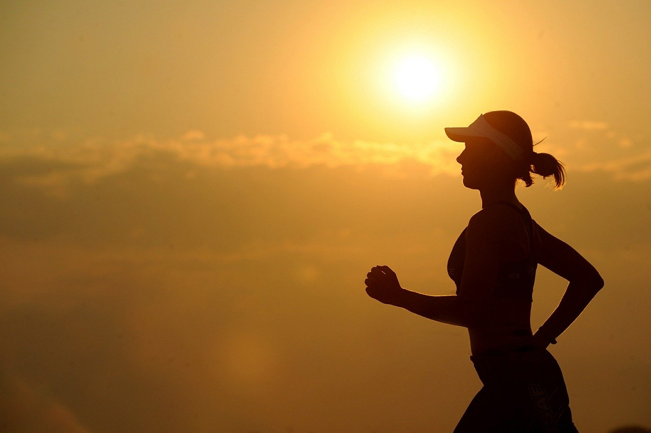 Silhouette of young woman jogging wearing a visor with setting sun in background