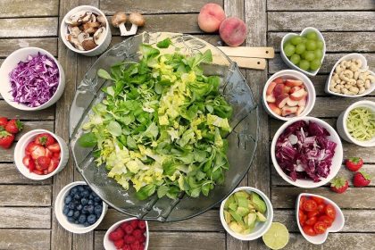 Large salad bowl with individual bowls of vegetables and toppings on a light wooden surface