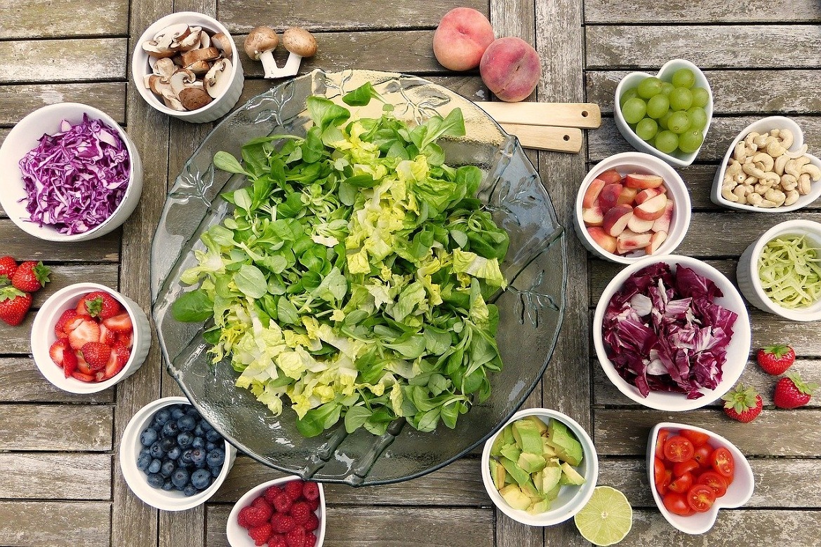 Large salad bowl with individual bowls of vegetables and toppings on a light wooden surface