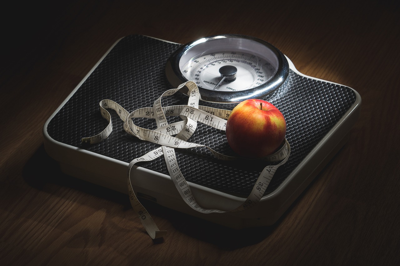 Black bathroom scale on dark wooden floor with red apple and tape measure for weight loss