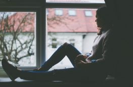 sad young woman quarantined sitting by window in a dark room looking outside