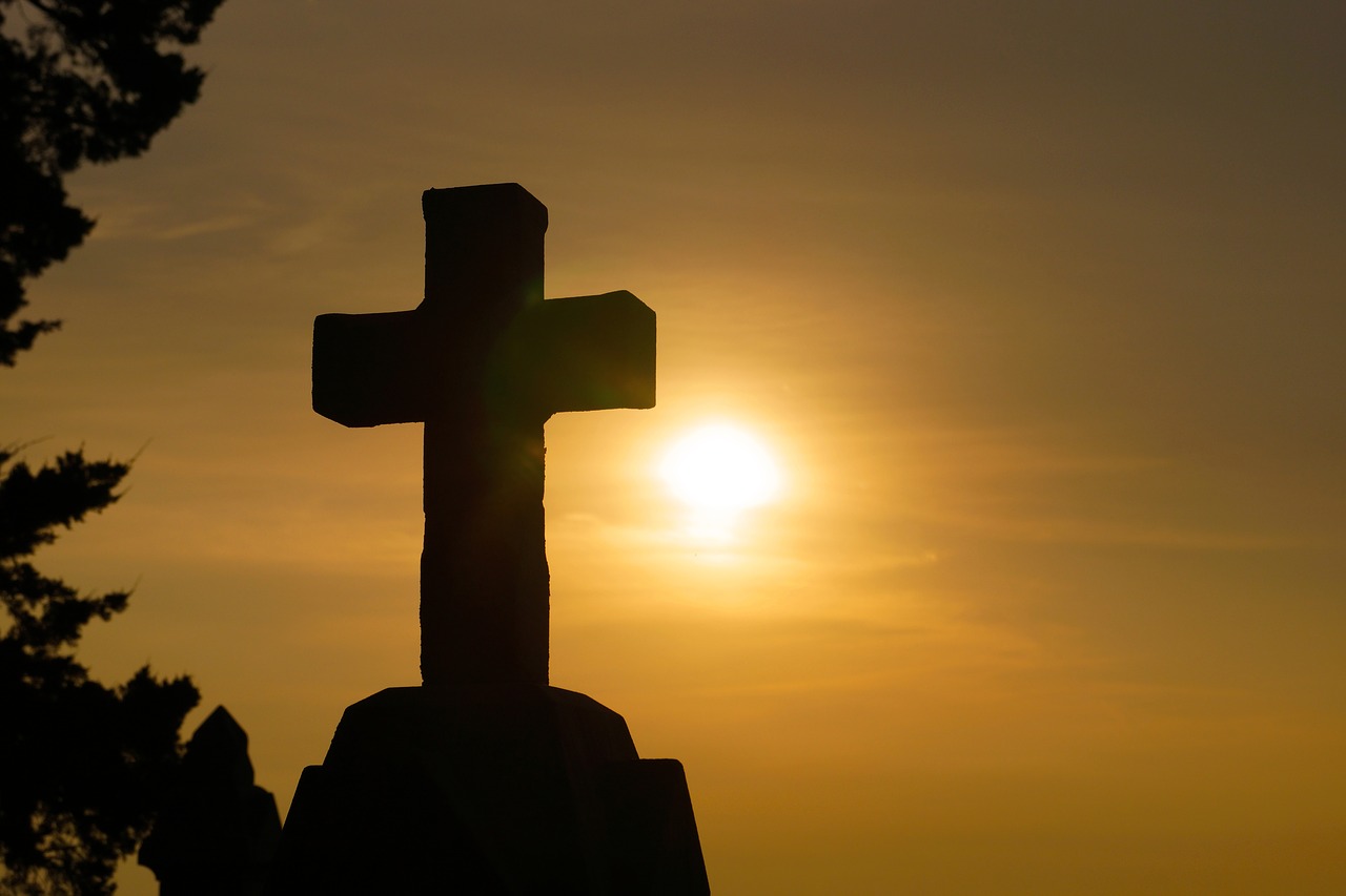 silhouette of large stone cross against hazy sunset sky