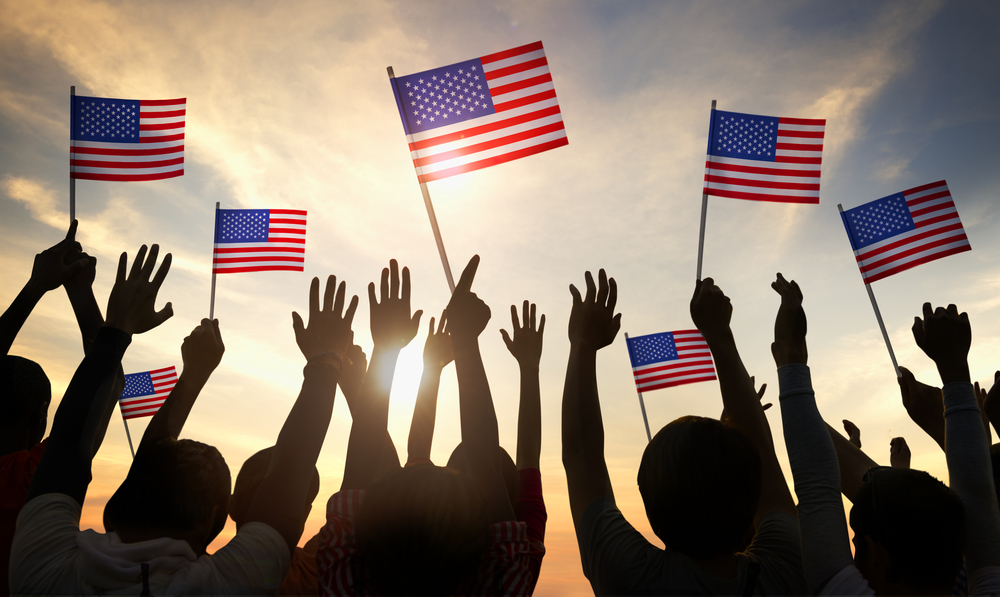 Silhouette of small crowd of people waving American flags in the sunset