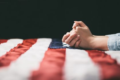Close-up of hands folded in prayer on American flag
