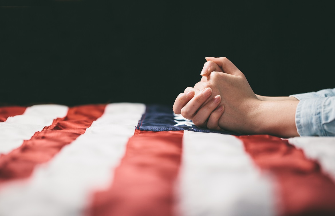 Close-up of hands folded in prayer on American flag