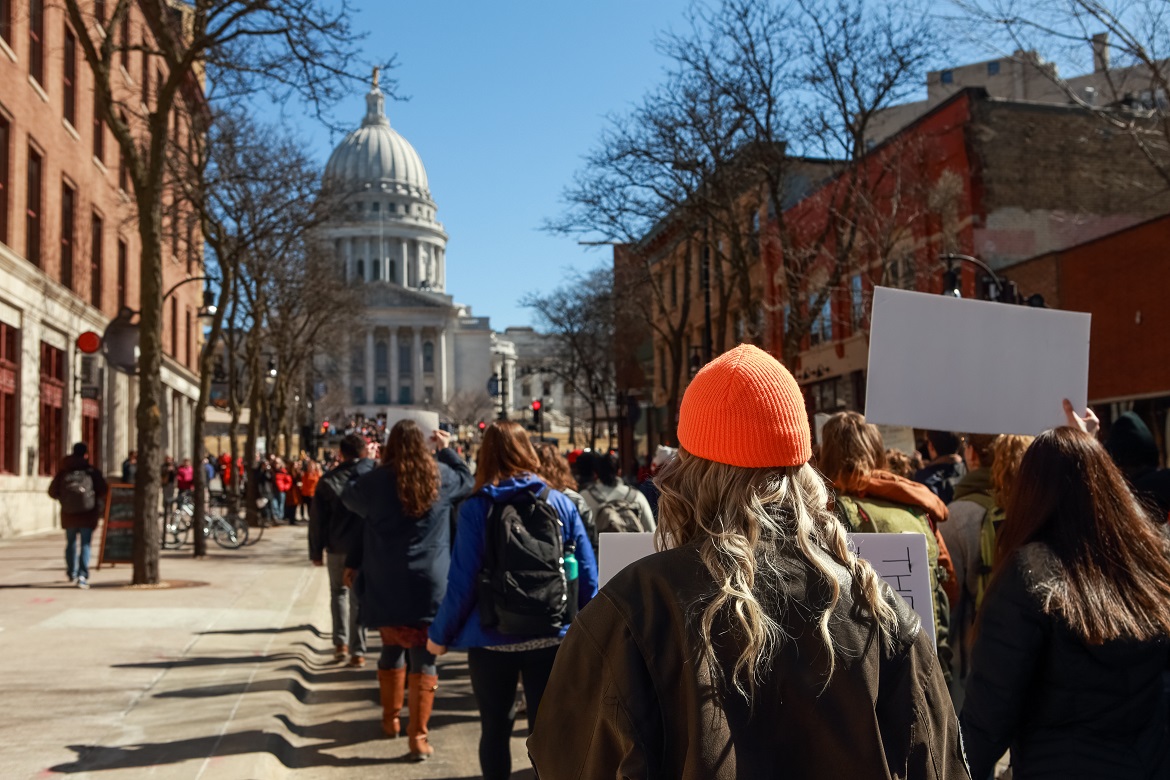 Crowd of young people holding signs marching on street near state capitol 