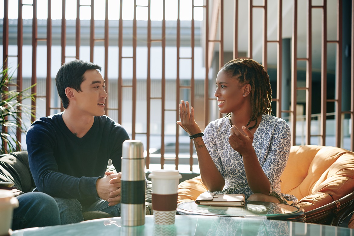 Smiling young black woman talking with young Asian man in an indoor cafe