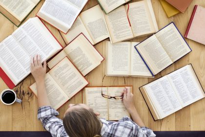 birds-eye view of young blond woman with open books spread out on a wooden tabletop