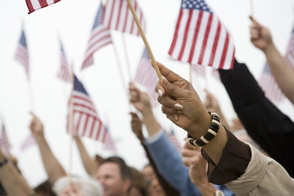 Americans of various races raising hands holding American flags