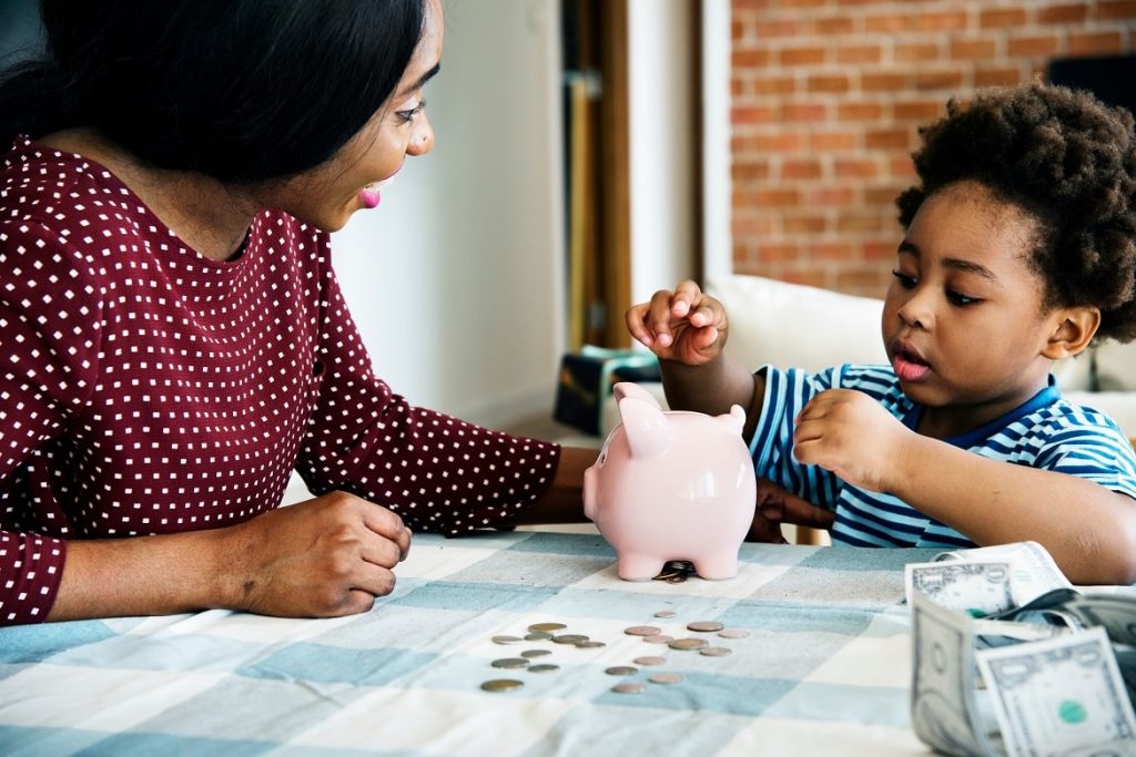Black mother helping son save money in a piggy bank.