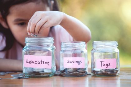 Little Asian girls placing coins in money budget jars.