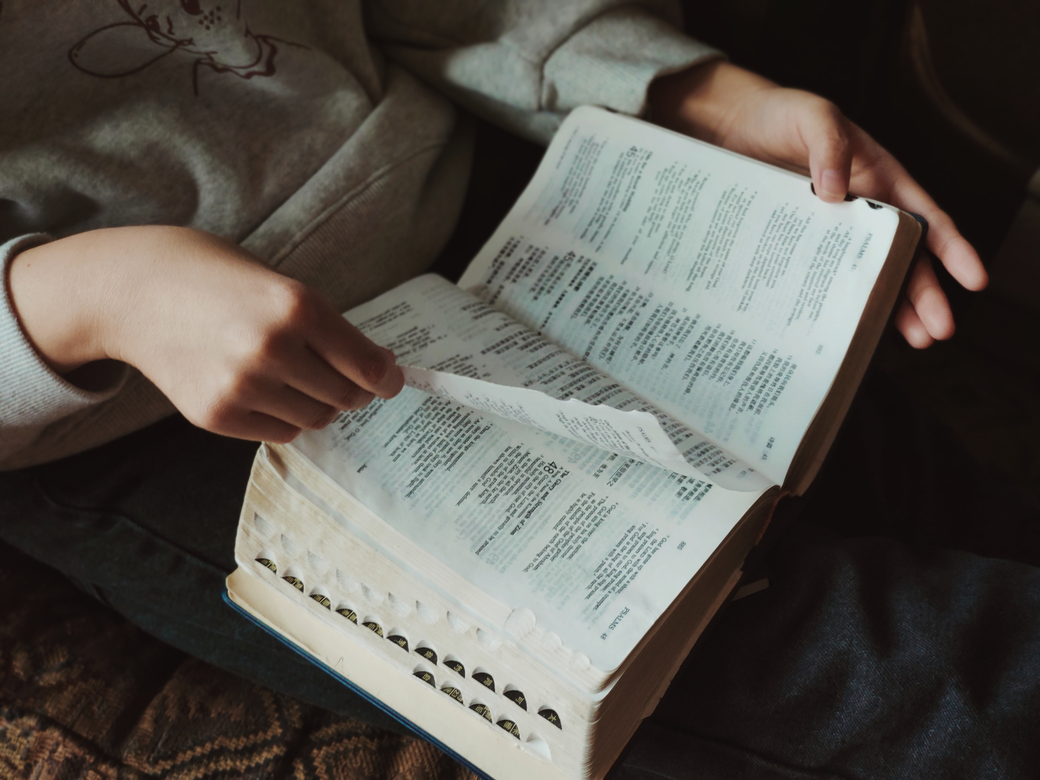 A person sits and reads their Bible, which we see in close up, on their lap. Reading the Bible with non-believer friends is a truly powerful way to share the good news with them.