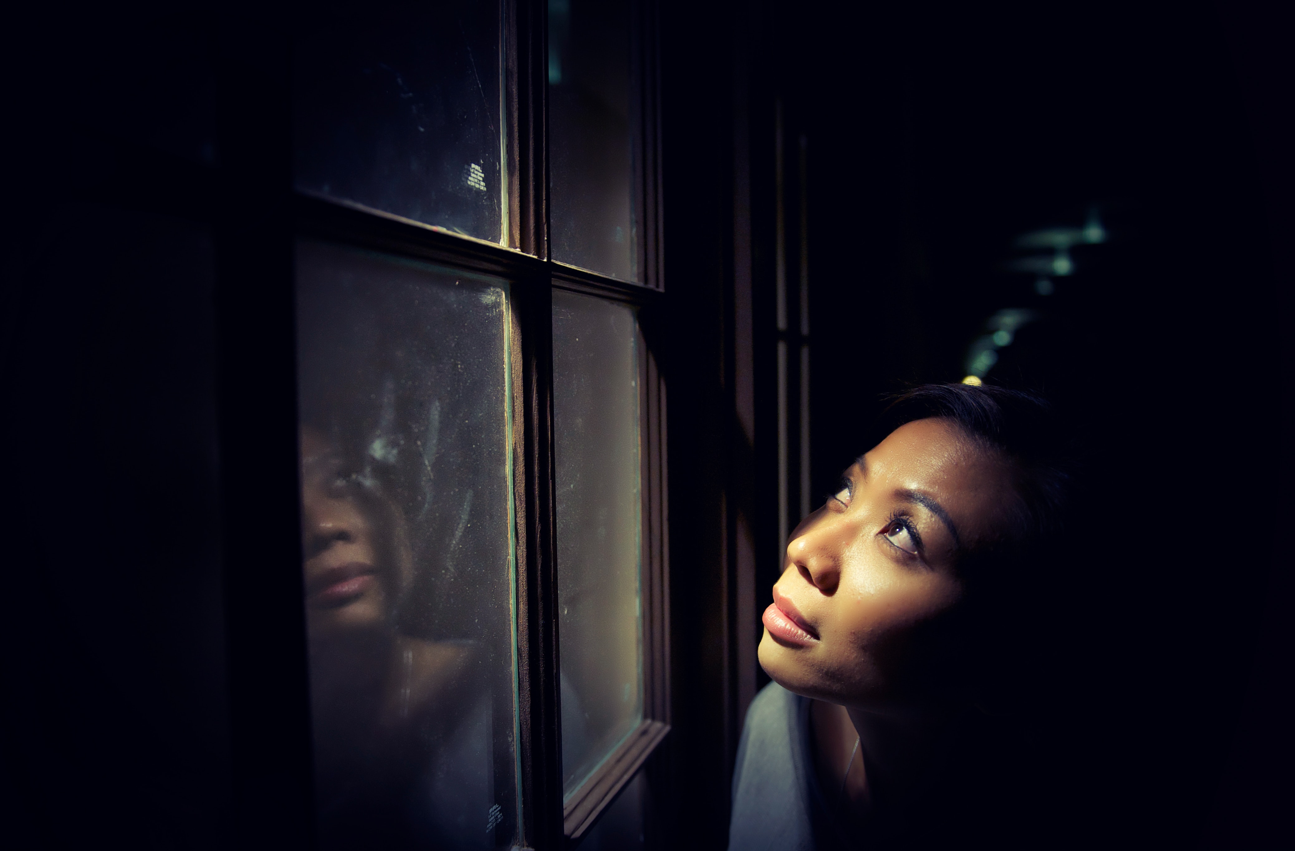 A woman looks towards the sky through a window. The light from the window illuminates her face and little else in a dim room. Her face looks hopeful. Can you really trust God? He leaves us signs all over the world that tell us you can trust Him!