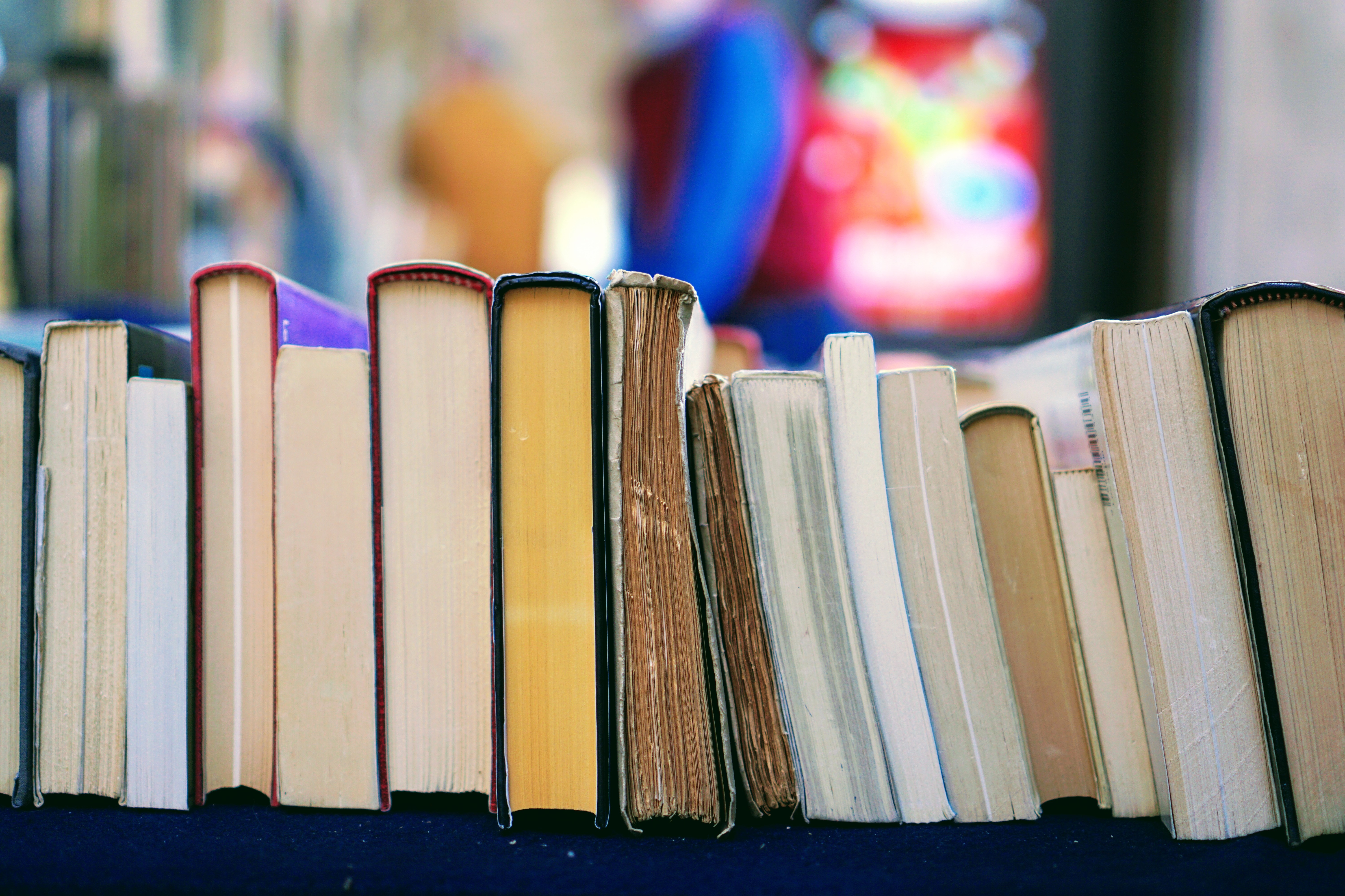 A stack of books lined up along a table with their spines facing up are seen in close up. There's no need to recreate a church experience when you meet with your non-believing friends, just reading a passage form the Bible and talking about it is all that is needed for God to begin his work in them.