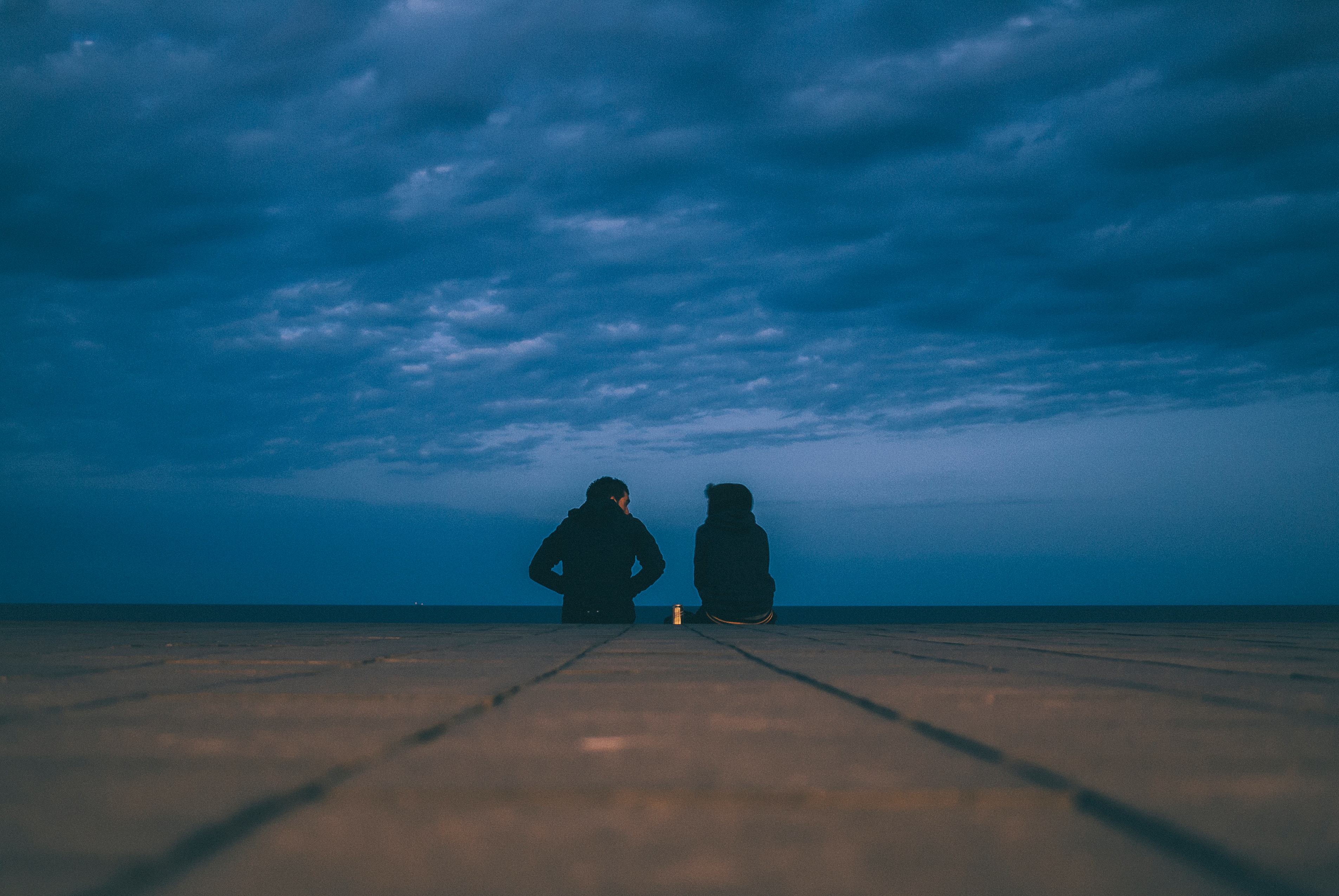 Two friends sit on the end of a dock, chatting with each other. They're wearing coats and the sky looks dark and moody. Who is seeking God's wisdom through you?