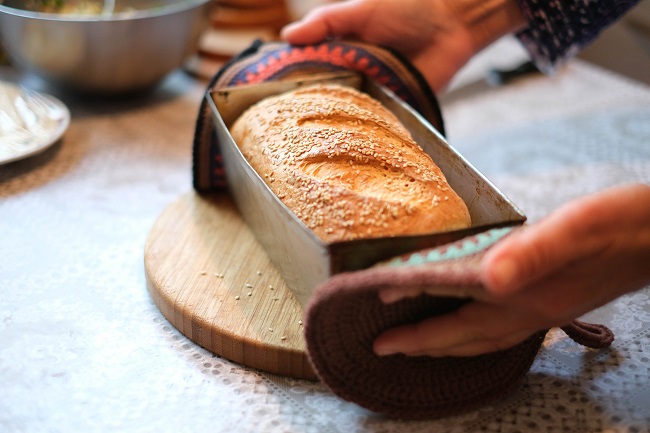 A pair of hands places a freshly baked loaf of bread, still in it's baking tin, on a table. The talent of cooking or baking pairs very well with the spiritual gift of hospitality!