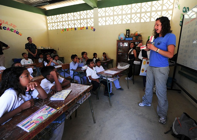 A yound woman stands in front of a class of boys and girls who are all watching her demonstrate something with an over-sized set of teeth. Spiritual gifts may lead us to teach, or they may lead us to support that teacher, something to consider when thinking about your gifts, is how God has wired your personality.