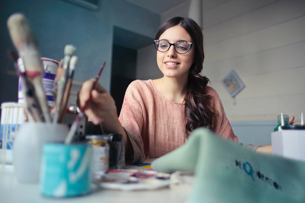 A young woman is clearly enjoying painting as she reaches for a color on the table with her paint brush. You can use creative spiritual gifts to help in ministry.