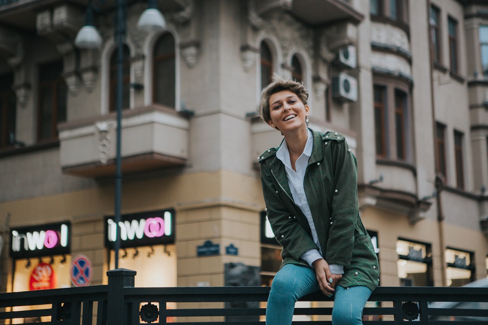 A young woman smiles as she sits on a metal fence in a city street. HEr spiritual gifts make her an extroarindary person in the Kingdom of God - how do your spiritual gifts make you extraordinary?