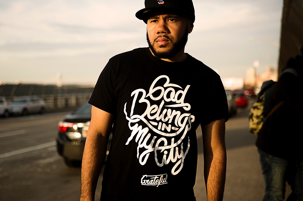 A young man in a black baseball cap and black slogan t-shirt, stands in the street. His t-shirt says 'God belongs in my city'. An ordinary person embracing the spiritual gifts God has given them, can become an extraordinary person in their use.