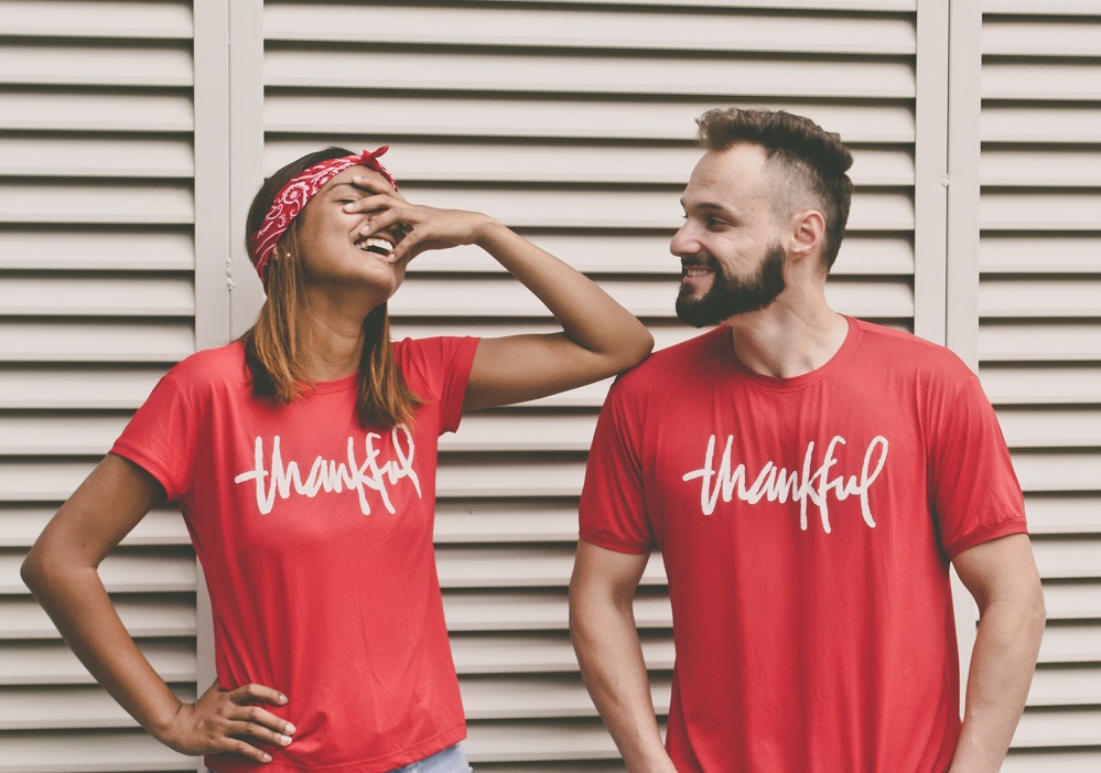 A man and a woman pose, laughing, in bright red t-shirts that say 'Thankful' on them. They become extraordinary when they use their own spiritual gifts in service.