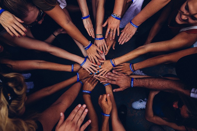 A large group of people all have their hands in for a team hand huddle. they're all working together, using their various spiritual gifts, for the good of the Kingdom!