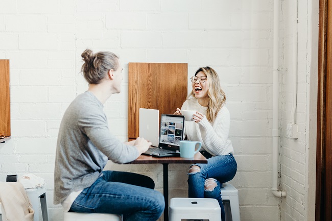 Two trendy friends sit opposite each other at a high top table. They both have laptops open in front of them, are drinking coffee and laughing together. Our spiritual gifts can be used in so many different ways, for many different ministries. It's up t you to discern where God wants you to use your spiritual gifts.