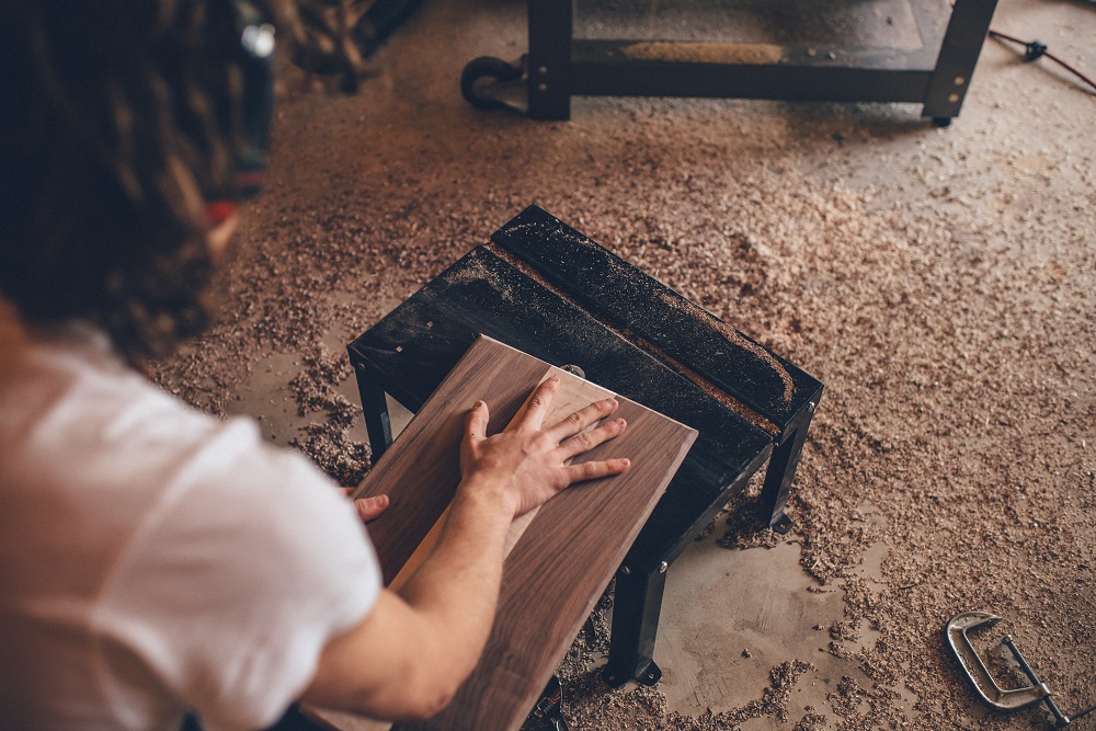 A carpenter moves a block of wood over a metal stool on the floor of his woodworking shop. He is using his spiritual gifts, and putting them to good use for the Kingdom.