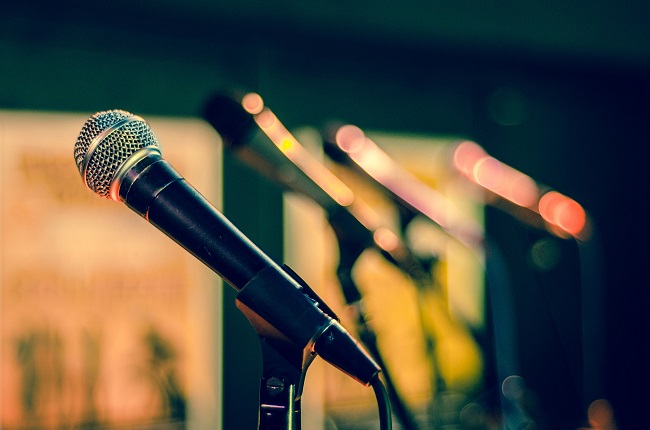 A microphone is photographed up close with a row of microphones behind it, out of focus and lit with beautiful, moody colors. Teaching is a spiritual gift and can involve speakign in front of lots of people, or just one person. It all counts!