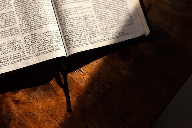 We see the lower half of and open Bible that is sat open on a wooden table with a shard of light lying across it. By reading our bible daily, we can know we are walking closely with God.