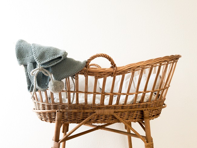 A wicker bassinet with white bedclothes and blue blanket hanging over the top end of it, is pictured against a white background. Why did Jesus come to us as a baby? this article seeks to answer that question.