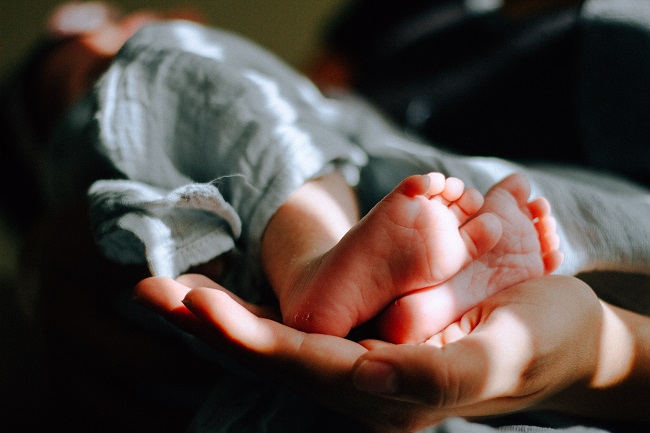 Tiny baby feet poke out from under a muslin blanket and an adult hand holds them up. We ask here, why did Jesus come to earth as a baby?