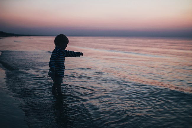 A toddler stands on the edge of the water on a beach at sunset. Why did Jesus come to Earth as a child?